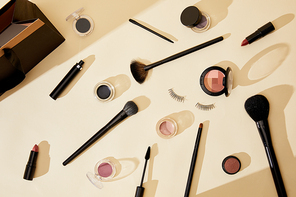 top view of different cosmetics and false eyelashes lying on beige tabletop