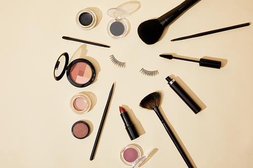 top view of different cosmetics lying on beige surface around false eyelashes