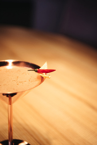 selective focus of alcoholic cocktail in metal glass decorated with chili pepper and nacho chip on wooden table