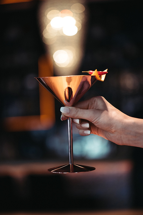 cropped view of woman holding alcoholic cocktail in metal glass decorated with nacho chip and chili pepper pn dark background