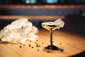 selective focus of alcoholic cocktail in metal glass decorated with orchid flower and coffee beans on dark background
