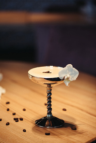 selective focus of alcoholic cocktail in metal glass decorated with orchid flower on wooden table