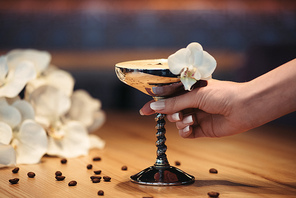 cropped view of woman holding alcoholic cocktail in metal glass decorated with orchid flower and coffee beans