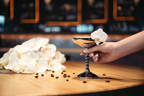 cropped view of woman holding alcoholic cocktail in metal glass decorated with orchid flower and coffee beans