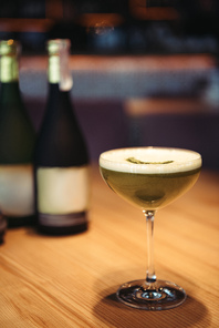 selective focus of delicious cocktail with foam on wooden table and bottles of champagne on background