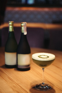 selective focus of delicious cocktail with foam on wooden table with bottles of champagne and copy space on background