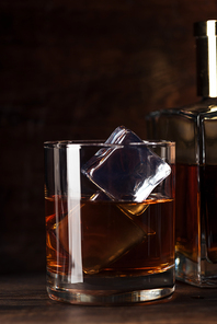 close-up view of glass of bourbon with ice cubes and bottle on wooden table