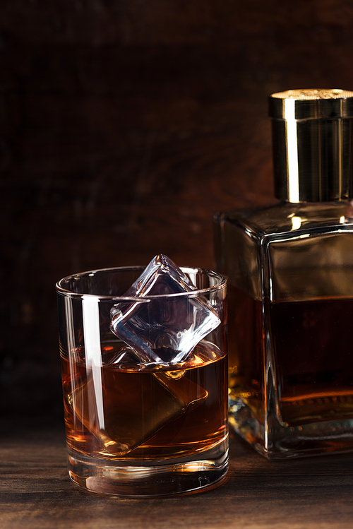 close-up view of glass of cognac with ice cubes and bottle on wooden table