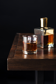 close-up view of glass and bottle of whisky on dark wooden table isolated on black