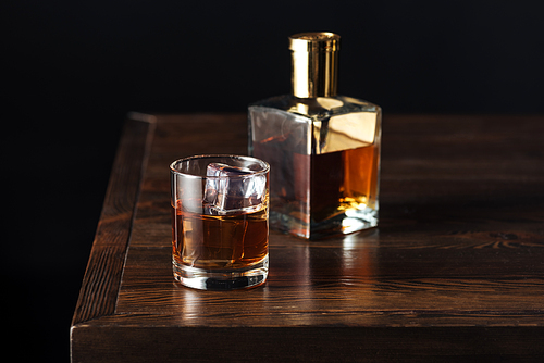 glass and bottle of whisky on dark wooden table isolated on black