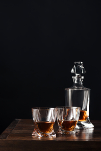 glasses and bottle of whisky on dark wooden table isolated on black