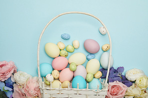 Top view of easter chicken and quail eggs in straw basket and flowers