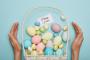 Cropped view of woman holding painted easter chicken and quail eggs in straw basket, card with happy easter lettering