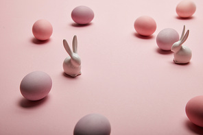 toy bunnies and painted easter eggs on pink background with copy space