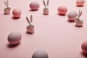 toy bunnies and painted easter eggs on pink background