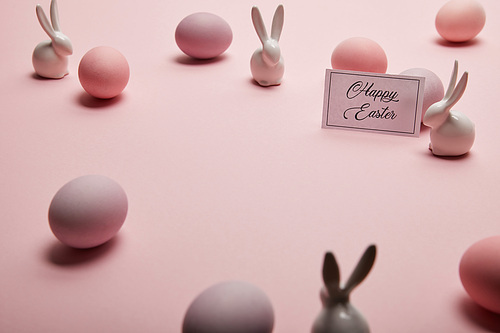 toy bunnies, card with happy easter lettering and easter eggs on pink background with copy space