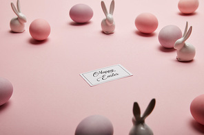 toy bunnies, card with happy easter lettering and painted easter eggs on pink background with copy space