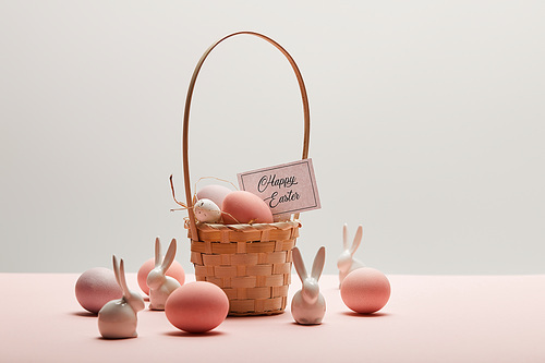 easter chicken and quail egg in straw basket, toy rabbits and card with happy easter lettering