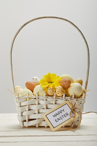 easter chicken and quail eggs in straw basket with flower and card with happy easter lettering on table