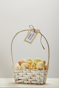 easter chicken and quail eggs in straw basket with flower and card with happy easter lettering