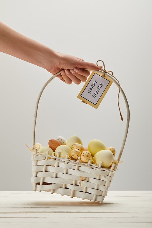 Cropped view of woman holding straw basket with easter chicken and quail eggs, card with happy easter lettering