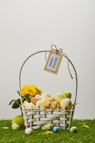 easter chicken and quail eggs in straw basket with flower and card with happy easter lettering on grass