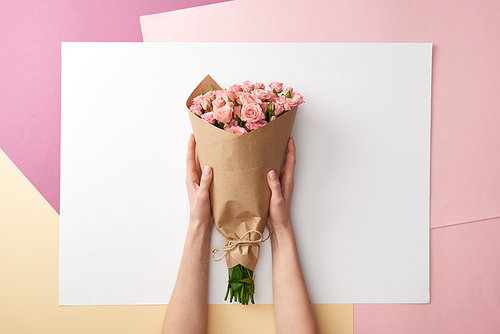 cropped shot of female hands holding bouquet of beautiful pink roses wrapped in craft paper