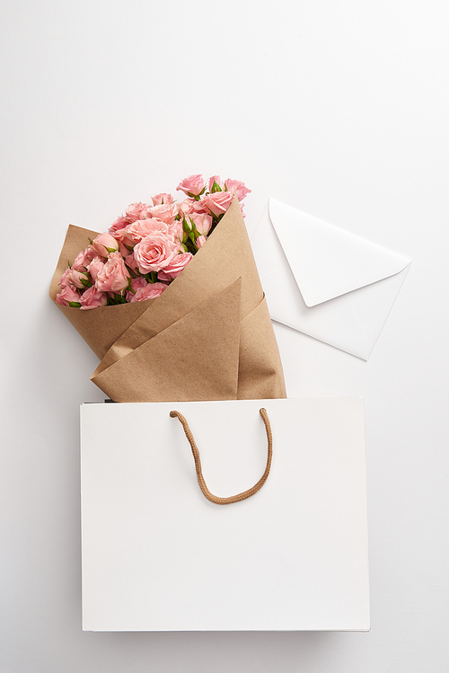 bouquet of beautiful pink roses and white envelope in paper bag on grey