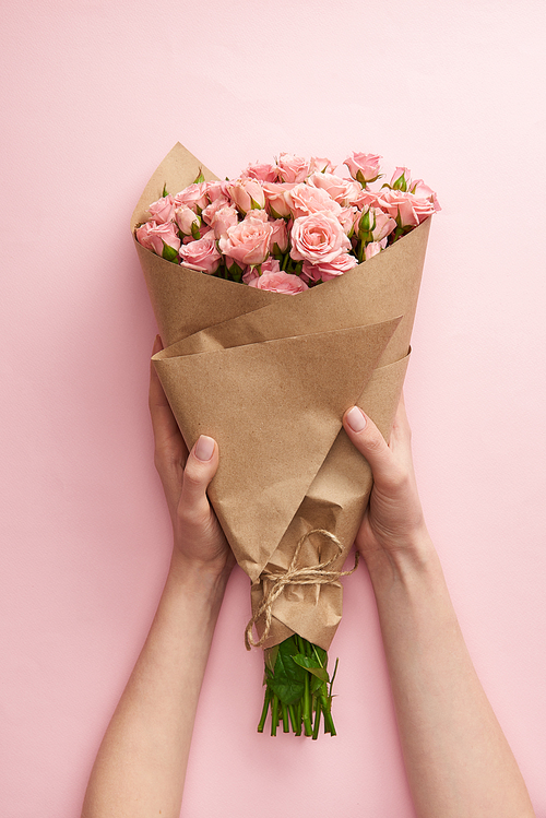 cropped shot of female hands holding bouquet of beautiful pink roses wrapped in craft paper on pink