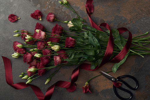 top view of beautiful eustoma flowers with ribbon and scissors on dark surface