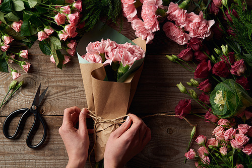 cropped shot of female hands typing rope on beautiful bouquet and tender flowers with scissors on wooden surface