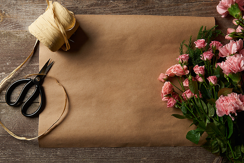 top view of beautiful pink flowers, scissors, ribbon and craft paper on wooden surface