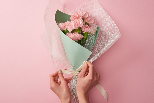 cropped shot of woman tying beautiful tender flower bouquet isolated on pink