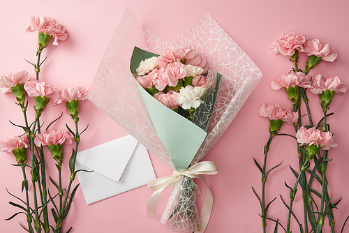 top view of beautiful bouquet, pink carnation flowers and white envelope isolated on pink
