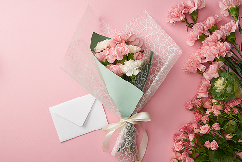 top view of beautiful tender flower bouquet and white envelope isolated on pink