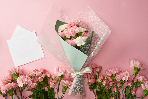 top view of beautiful bouquet, tender pink flowers and white envelope with card isolated on pink