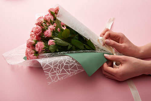 cropped shot of woman wrapping beautiful tender roses on pink