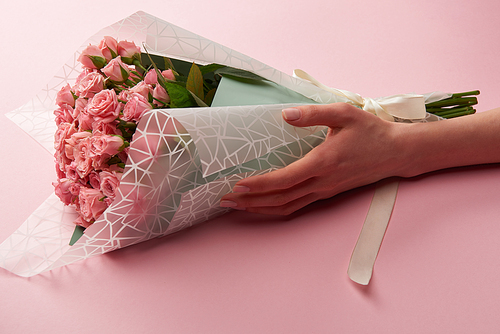 cropped shot of female hand and beautiful pink roses bouquet on pink