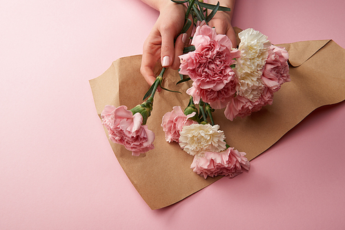 cropped shot of woman wrapping beautiful flowers in craft paper on pink