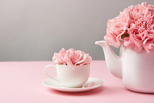 close-up view of beautiful tender pink flowers in white teapot and cup on grey