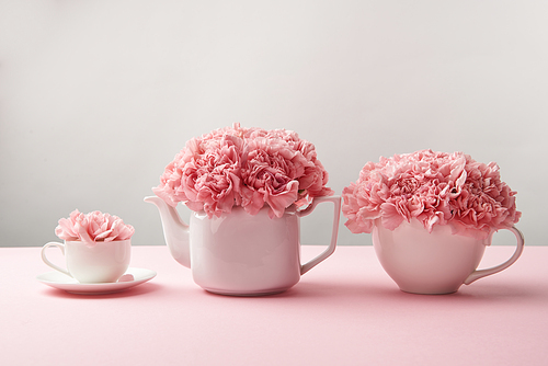 beautiful tender pink flowers in white teapot and cups on grey