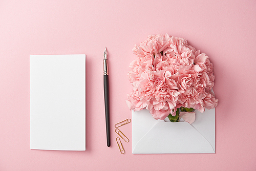 top view of blank card, ink pen and pink flowers in white envelope isolated on pink