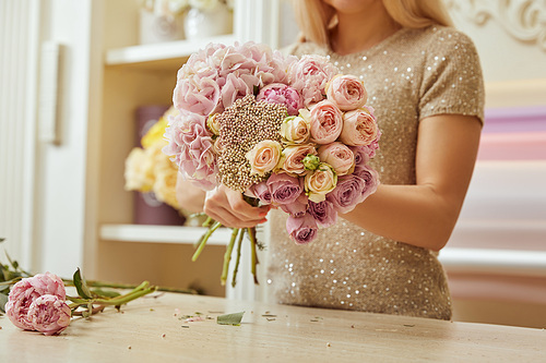 partial view of florist making bouquet of roses and peonies at workplace