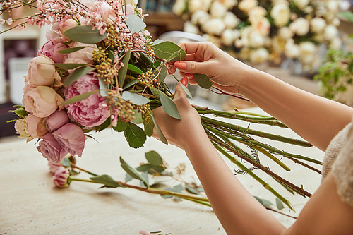 florist making bouquet of roses and peonies at workspace