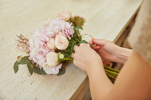 partial view of florist making bouquet of beige roses and peonies at workspace