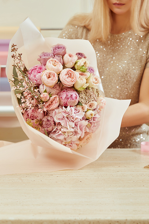 partial view of florist wrapping with paper bouquet of roses and peonies at workspace