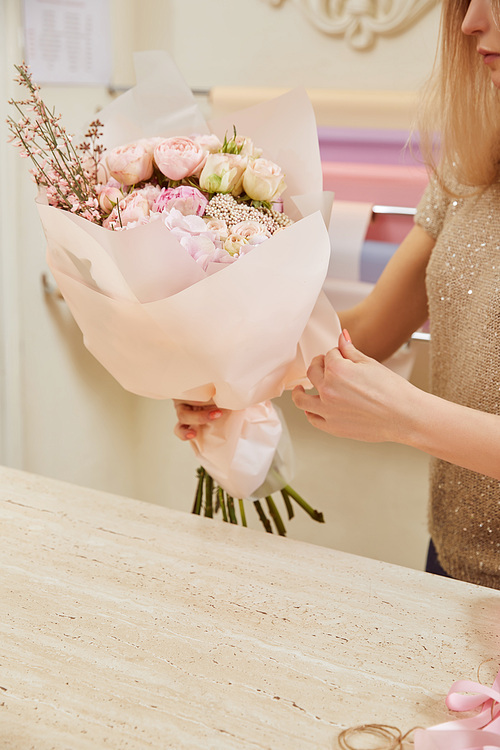 partial view of florist holding bouquet of roses and peonies at workspace