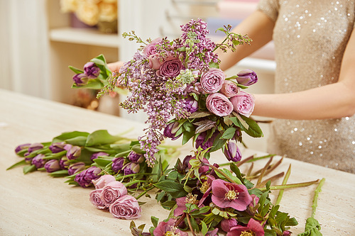 partial view of florist making bouquet of tulips, peonies and lilac at workplace