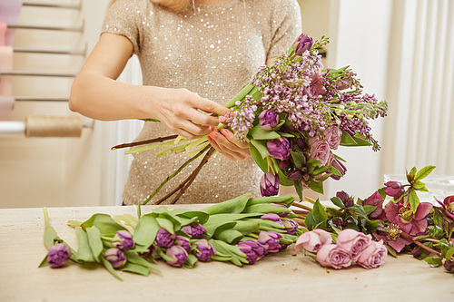 partial view of florist making bouquet of tulips, peonies and lilac at flower shop