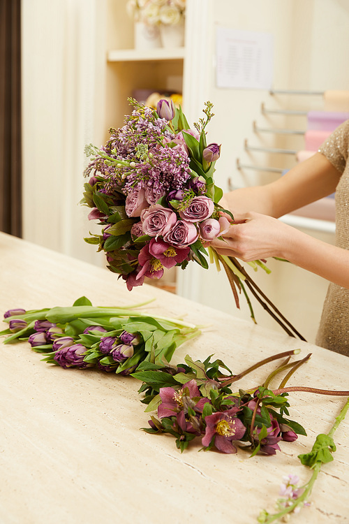 cropped view of florist making bouquet of tulips, peonies and lilac at workplace